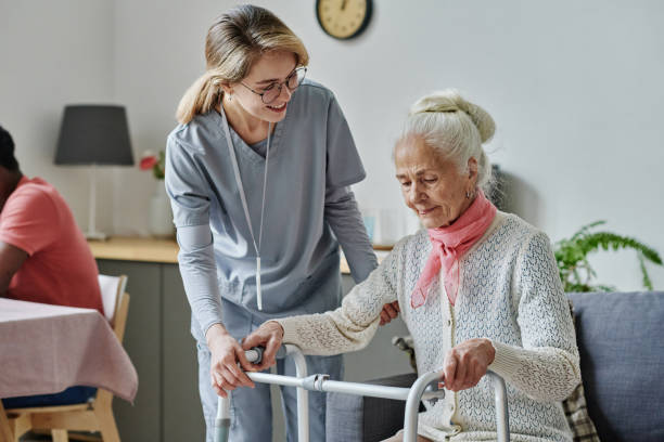 Young caregiver caring about senior woman Young caregiver caring about senior woman in nursing home, she helping her to stand using walker nursing home stock pictures, royalty-free photos & images