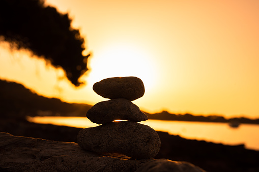 Piled up Zen stones on real sunrise in front of the sea. Strong backlighting and possible noise. For zen, mindfulness and other spiritual concepts.