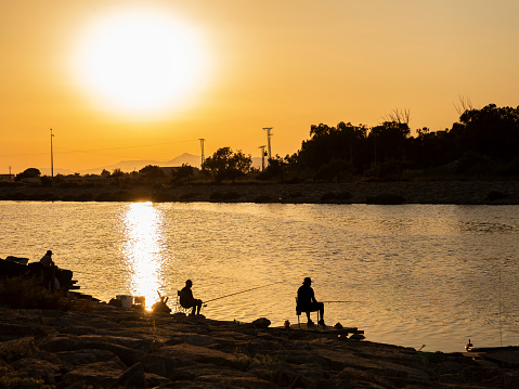 golden landscape with people fishing in the river at sunset