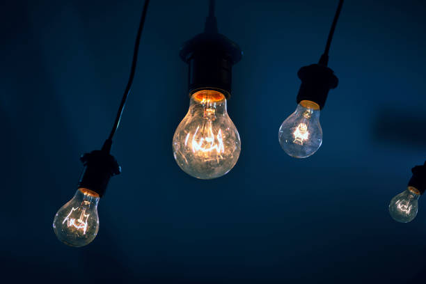 four lighted light bulbs hanging on a blue background. concept of energy consumption