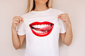 Young blonde woman shows her white casual t-shirt with trendy creative design of big smiling mouth