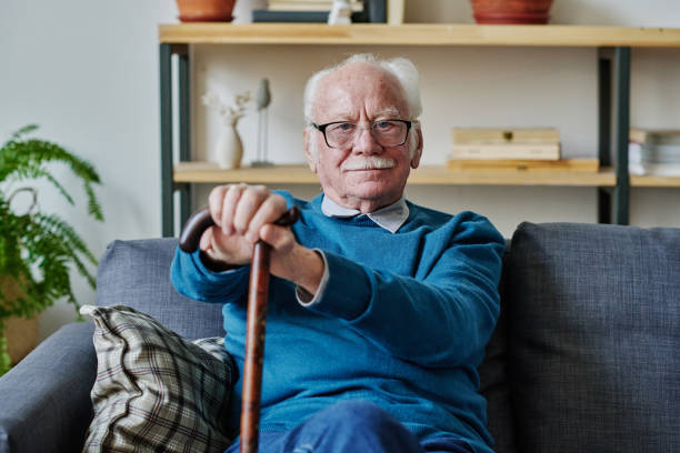istock Senior man with stick sitting on sofa 1457905925