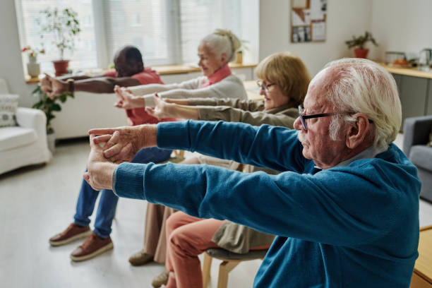 Senior people doing exercises in the morning Side view of senior people doing exercises sitting on chairs in the morning in the room nursing home stock pictures, royalty-free photos & images