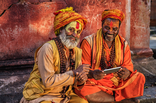 Sadhu - indian holymen using the mobile phone. In Hinduism, sadhu, or shadhu is a common term for a mystic, an ascetic, practitioner of yoga (yogi) and/or wandering monks. The sadhu is solely dedicated to achieving the fourth and final Hindu goal of life, moksha (liberation), through meditation and contemplation of Brahman. Sadhus often wear ochre-colored clothing, symbolizing renunciation.