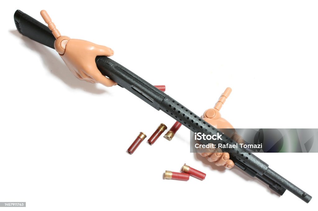 Action figure hand holding weapon in a white background Small plastic hand holding a shotgun. Model scale toy in close up macro. Small red cartridge shells Action Figure Stock Photo