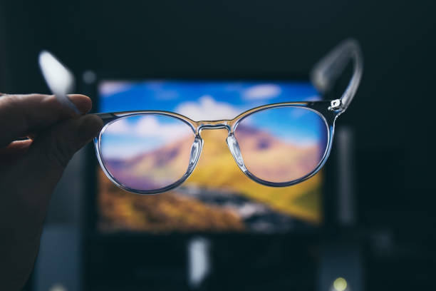 Selective focus on transparent clear blue light computer glasses and computer screen glowing on the background in home or office. Blue light glasses protect eyes and eyesight from screens blue light. stock photo