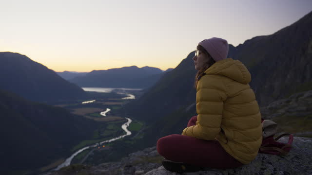 Woman sitting on the rock and looking at scenic view of mountains while hiking