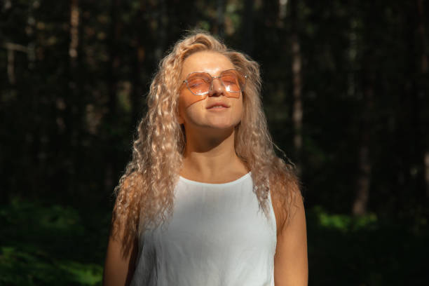 The young woman in sunglasses looking at the sun against the background of a dark forest stock photo