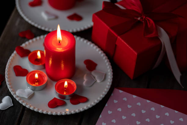 istock Saint Valentine's Day celebration. Red burning candles, hearts, gift box, postcard on dark wooden background. Happy holiday . Table decor for festive dinner, romantic atmosphere 1457921925