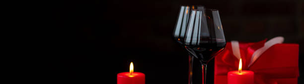 istock Saint Valentine's Day celebration. Wineglasses with red wine, hearts, gift box, postcard on dark wooden background. Happy holiday . Table decor for festive dinner, romantic atmosphere. Banner copy space 1457922086