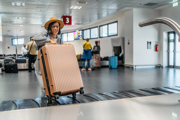 młoda kobieta odbiera bagaż z karuzeli bagażowej na lotnisku - luggage ramp zdjęcia i obrazy z banku zdjęć