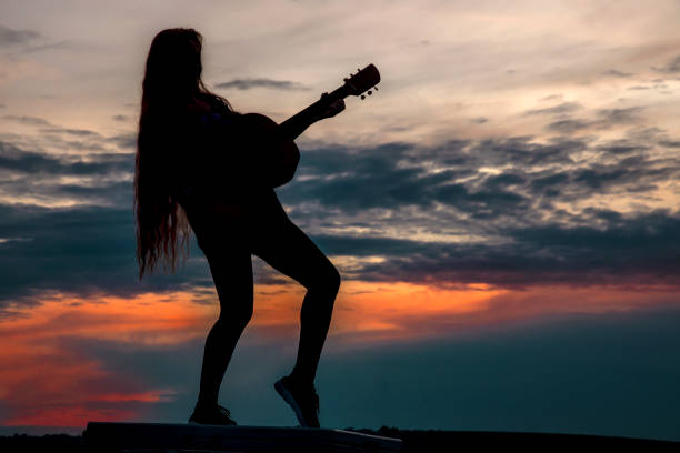 istock Silhouette woman playing guitar in sunset 1457927542