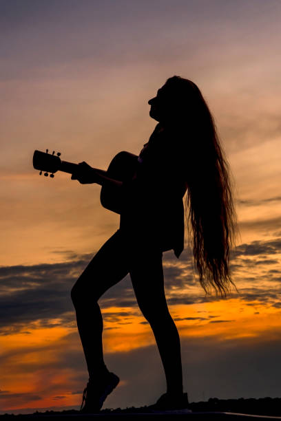 Silhouette woman playing guitar in sunset