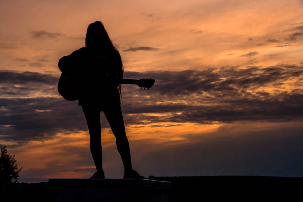istock Silhouette woman playing guitar in sunset 1457927560