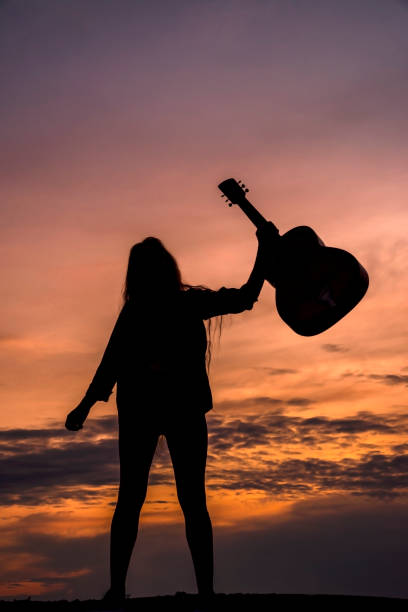 istock Silhouette woman playing guitar in sunset 1457927562
