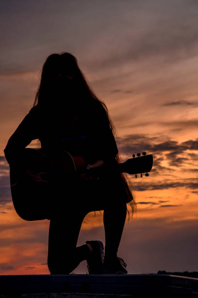 istock Silhouette woman playing guitar in sunset 1457927567