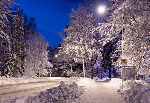 City road and footpath in Finland Lahti, Mukkula. Winter night landscape, snow-covered road and trees covered with snow.