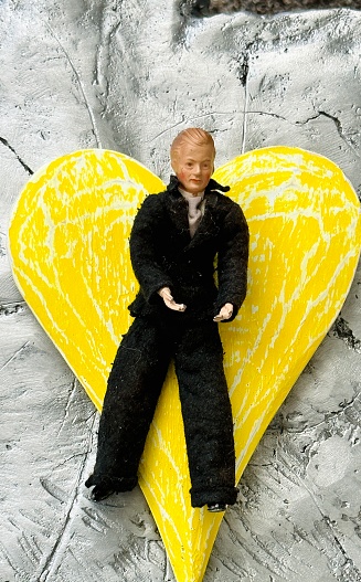 Vintage puppet, black dressed man lying on a yellow heart shape