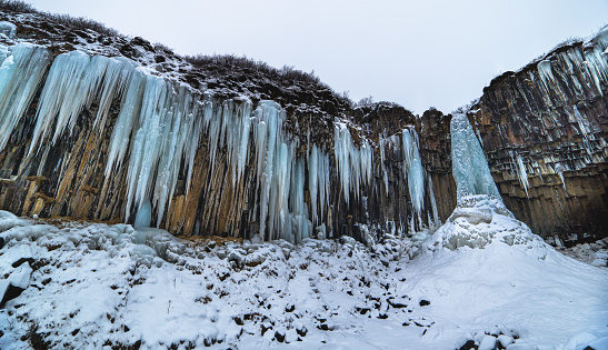Svartifoss iceland black waterfall completely frozen with bluish stalactites and snow under white sky