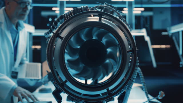 Zoom Out Footage From Inside an Advanced Turbine Engine with Rotating Fan. Adult Engineer with Laptop Computer Comes Up to Perform Diagnostics and Sustainability Tests on the Motor