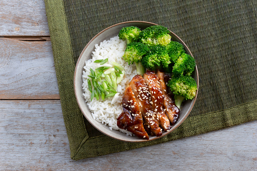 Japanese dish katsu chicken curry with vegetables: broccoli, red and yellow sweet pepper and parsley over jasmine rice served on a pink plate on a stone background served with chopsticks, close-up