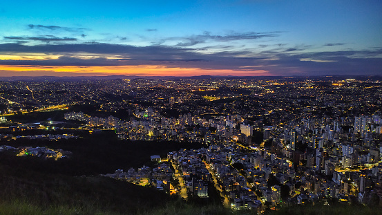 Dusk with sunset in the city of Belo Horizonte, in the state of Minas Gerais, seen from the top of a mountain that is within the city. This mountain is in the extreme west and allows a wide view of the entire metropolitan region. The city lights extend to the horizon and in the foreground is the Buritis neighborhood.