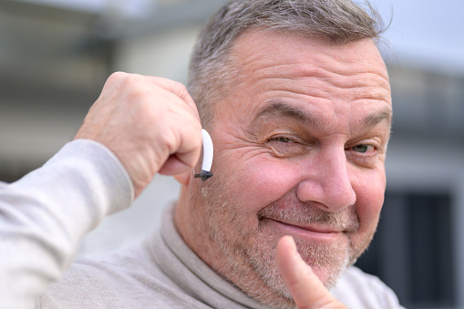 Portrait of a middle aged grey-haired hard of hearing man in his fifties or sixties with a hearing aid in his ear giving a thumbs up