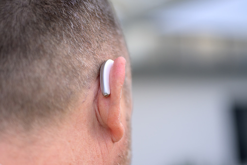 Rear view of a middle aged gray haired hard of hearing man in his fifties or sixties with a hearing aid in his ear