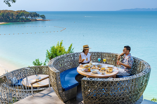 couple having lunch at a restaurant looking out over the ocean of Pattaya Thailand, man and woman having dinner in a restaurant by the ocean in Pattaya.