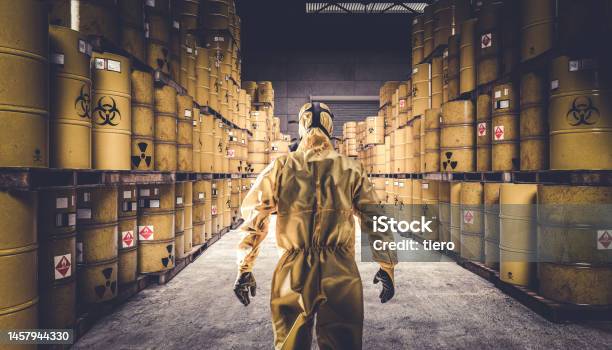 Man In Yellow Protective Suit And Gas Mask Warehouse Full Of Yellow Metal Barrels Stock Photo - Download Image Now