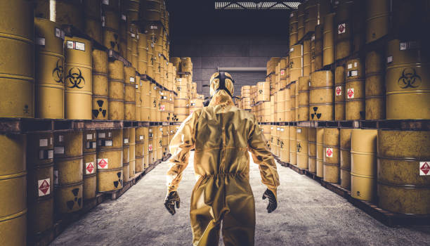 man in yellow protective suit and gas mask, warehouse full of yellow metal barrels - medical waste imagens e fotografias de stock