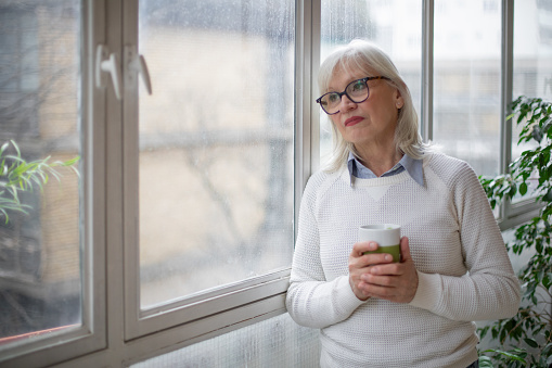 mature woman having a cup of tea, leaning on a window