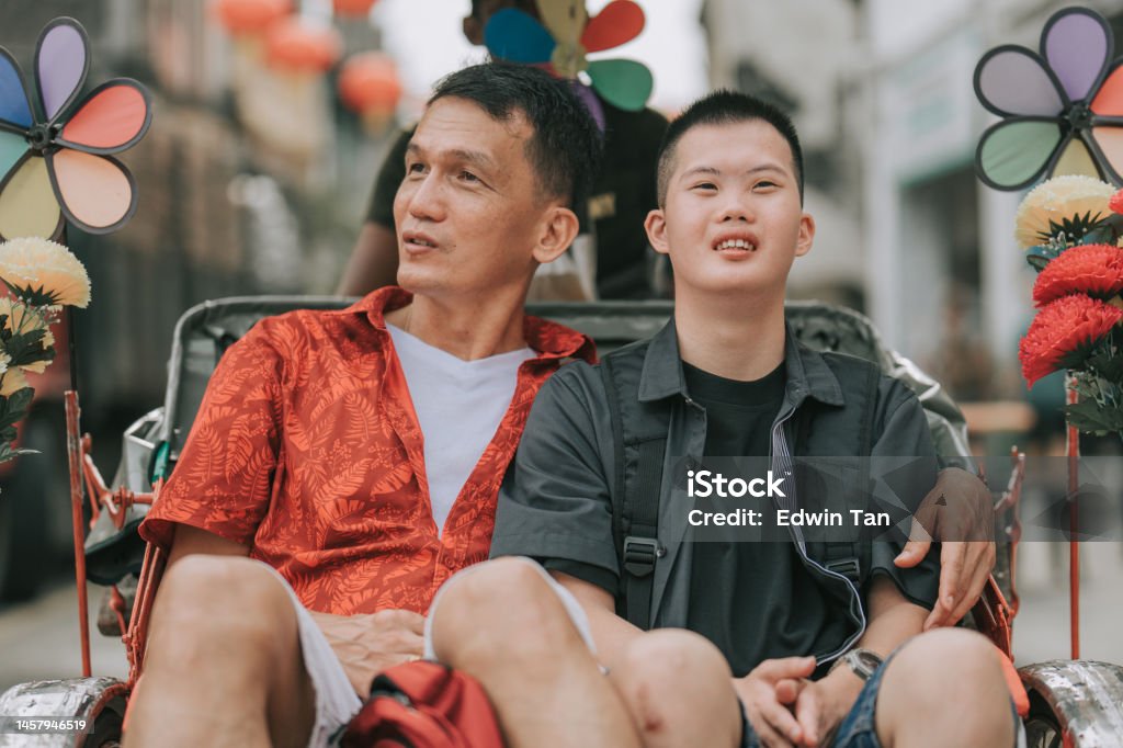 Asian Chinese down syndrome young man enjoying rickshaw ride in Penang street with father Active Lifestyle Stock Photo