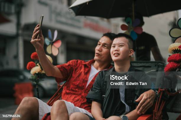 Asian Chinese Down Syndrome Young Man Enjoying Selfie Rickshaw Ride In Penang Street With Father Stock Photo - Download Image Now