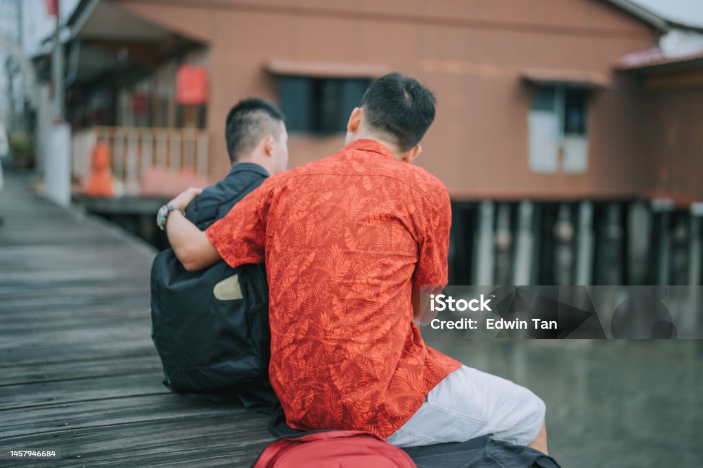 Asian Chinese father talking t o down syndrome son siting on footbridge in Penang travel Rear View Stock Photo