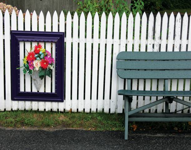 Framed bouquet of flowers hangs on white fence next to park bench in Chatham, MA