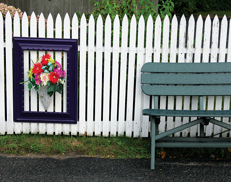 Framed bouquet of flowers hangs on white fence next to park bench in Chatham, MA