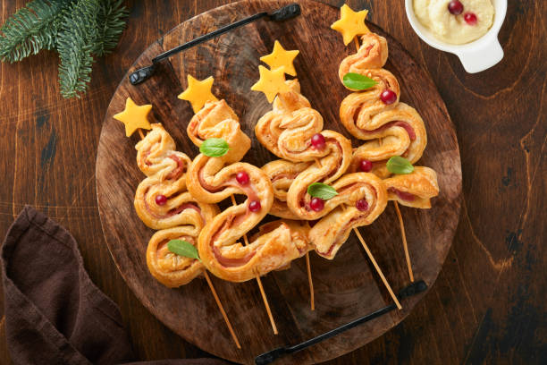 istock Christmas or New Year appetizer. Christmas tree shape puff pastry buns with cheese and ham. Group of Christmas tree shapes on wooden board. Festive idea for Christmas or New Year dinner. Top view. 1457948587