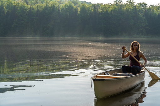 A Portuguese woman canoeing on a lake of the Laurentians,  Quebec, during a sunrise of summer.