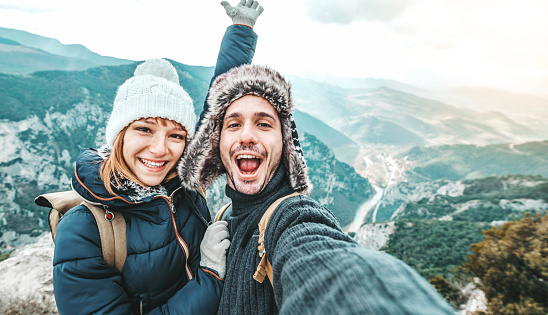 Happy couple of hikers taking selfie picture on top of the mountain - Two travelers with backpack smiling together at camera - Travel blogger influencer streaming using smart mobile phone device