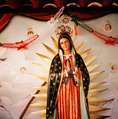 A small statue of the virgin of Guadalupe in a church. \nShe holds a special place in the culture and religious life of many Mexicans and Mexican American and was said to appear before a young boy in the 16th century