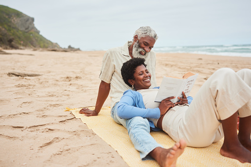 Smiling mature woman reading a book while lying on her husband's lap during a day on a sandy beach