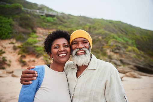 Portrait of a smiling mature couple standing arm in arm together on a sandy beach on an overcast day