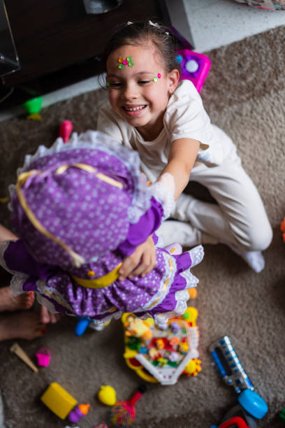 Latina girl, 8 years old, dressed comfortably, is playing in the living room of her house, with her dolls, while behind her is her family gathered on the sofa