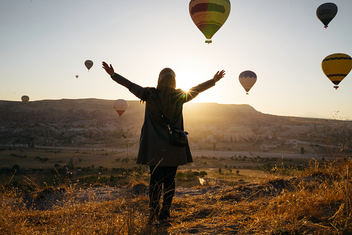 woman enjoy the sunrise with view of  hot balloon in goreme
