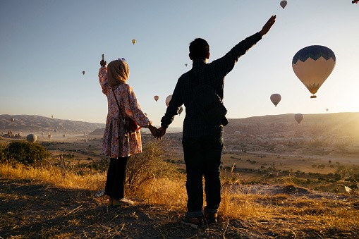young muslim couple enjoy the sunrise with view of  hot balloon in goreme