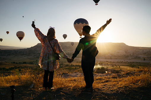 young muslim couple enjoy the sunrise with view of  hot balloon in goreme