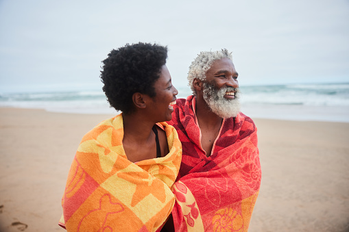 Laughing mature couple wrapped in towels walking along a beach after a swim in the ocean