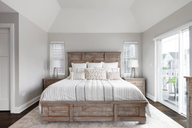 A bedroom with a wood headboard and footboard. A beautiful bedroom with natural wood furniture, a glass door leading to a outdoor patio, and a cathedral ceiling. bedroom stock pictures, royalty-free photos & images