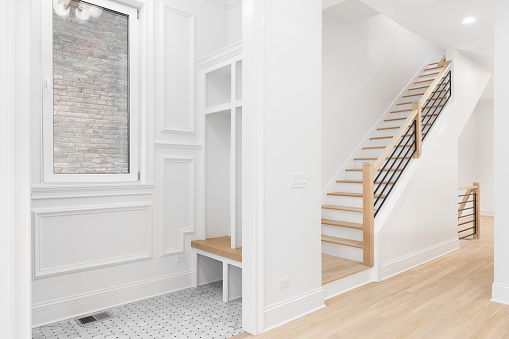 An entryway with a bench, shelving, and tiled flooring looking towards a staircase with wood railing, hardwood floor, and wrought iron spindles.